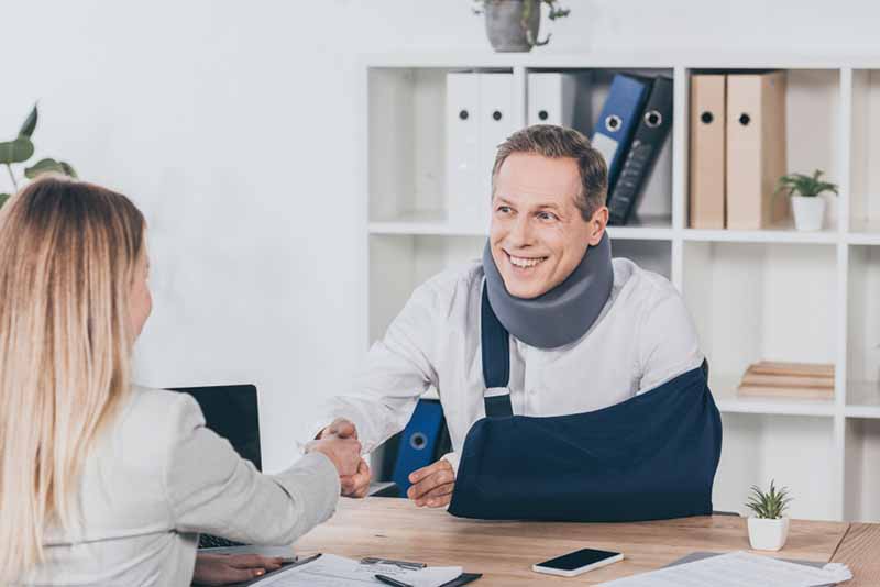 lawyer shaking hands with worker in neck brace and arm bandage over table in office, 